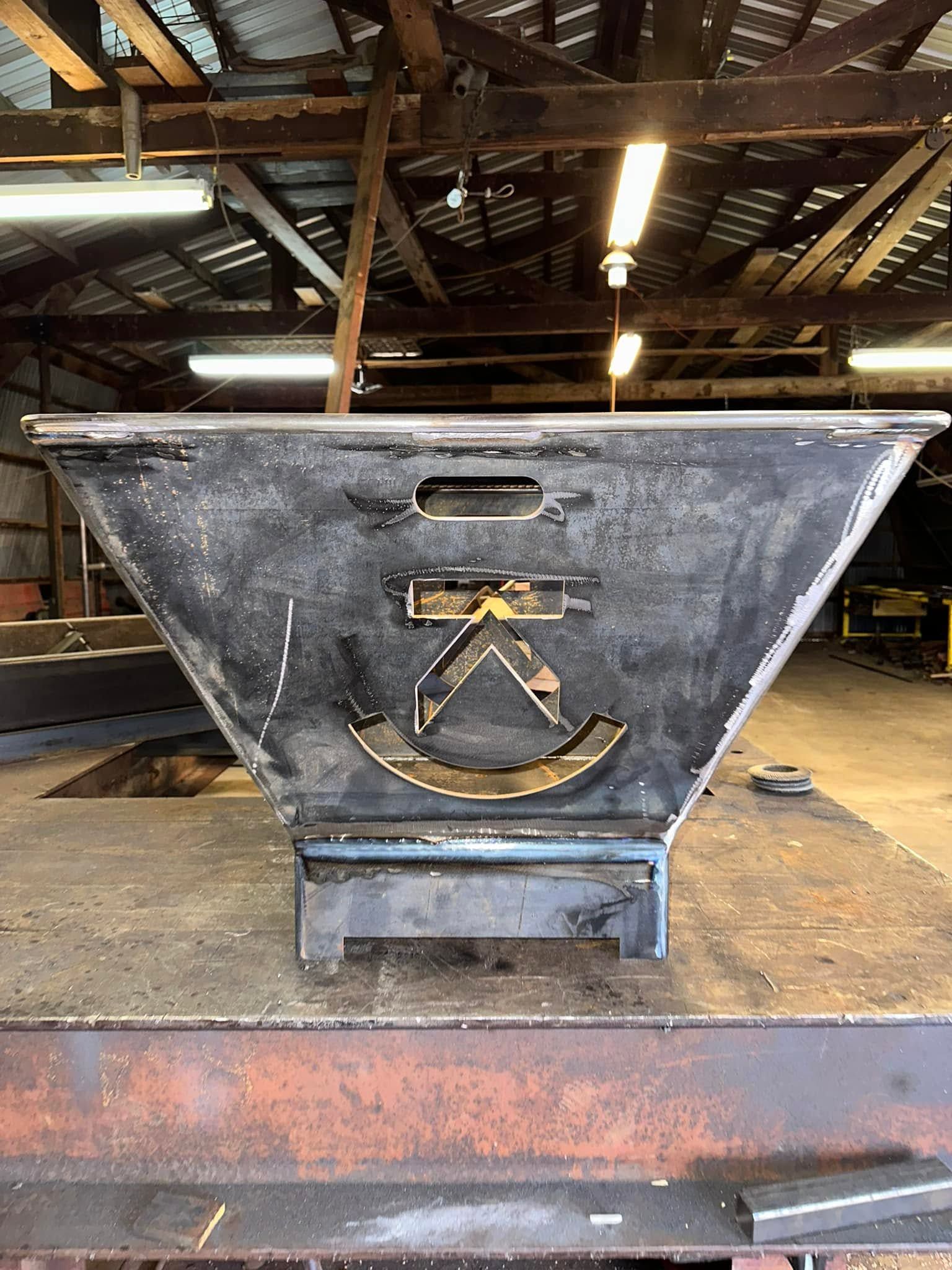 Rusty metal hopper with a logo, sitting in an industrial workshop