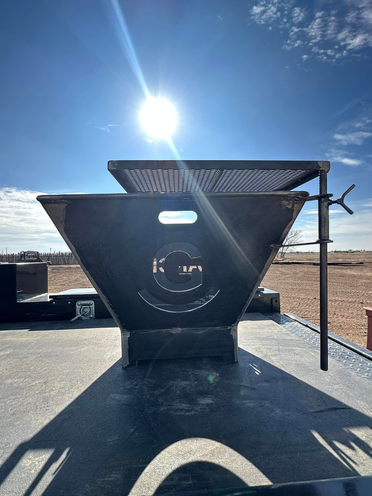 Large black metal grill or fire pit outdoors under a bright sun, with desert landscape in the background