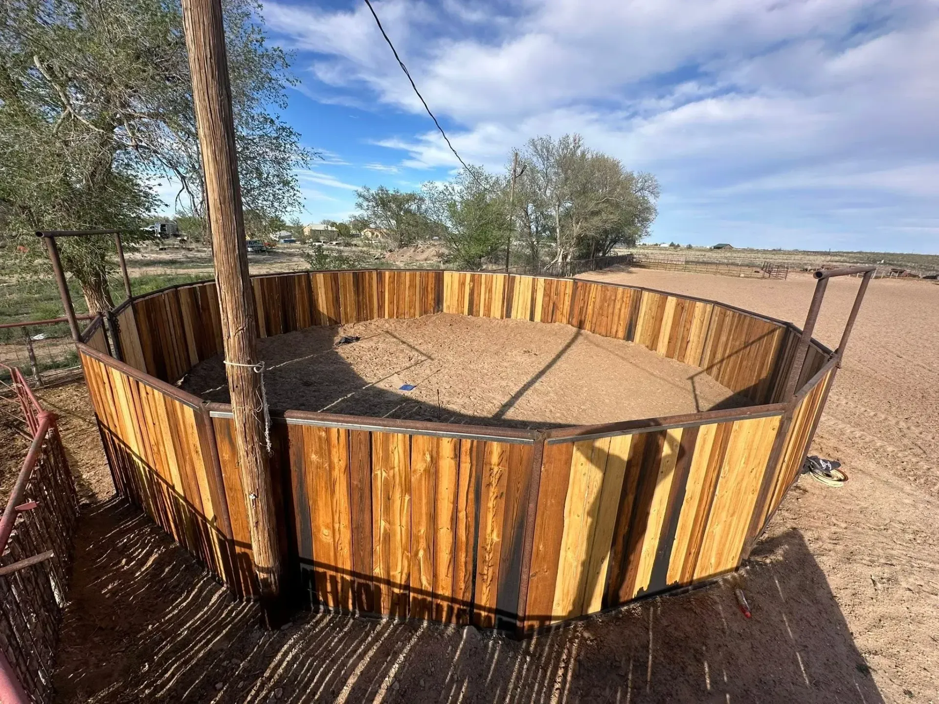 Round wooden animal pen in a dusty outdoor yard with a tree inside