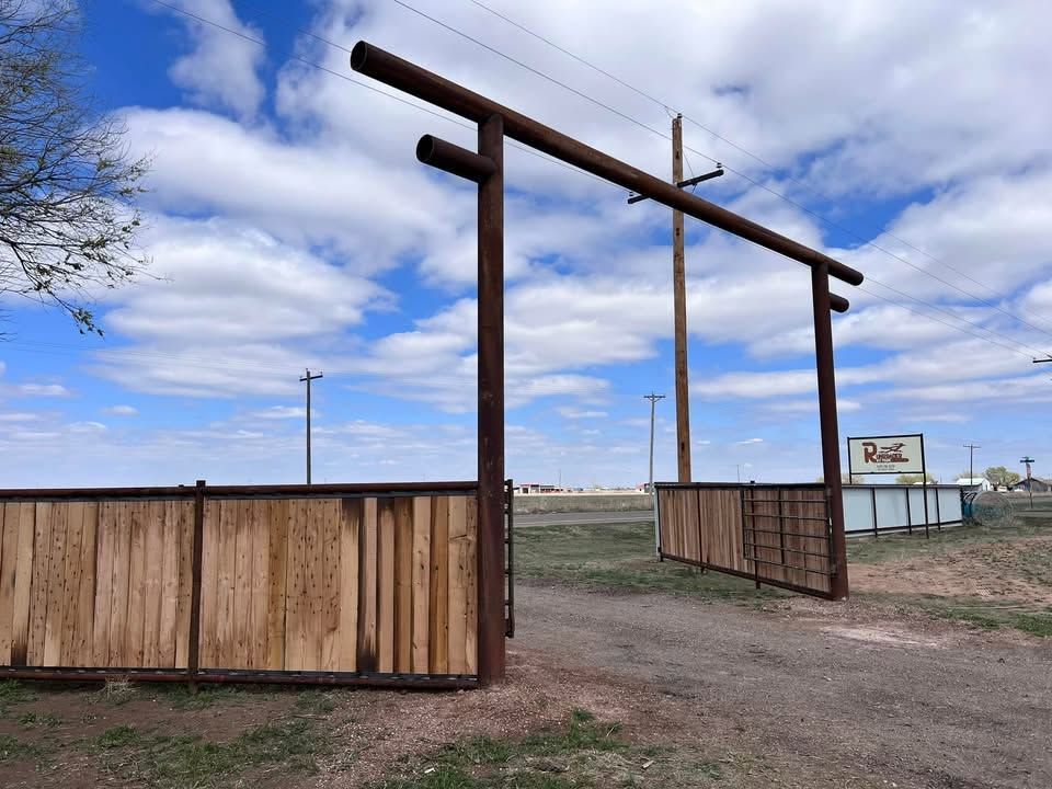 Open wooden gate to a dirt road under a blue sky