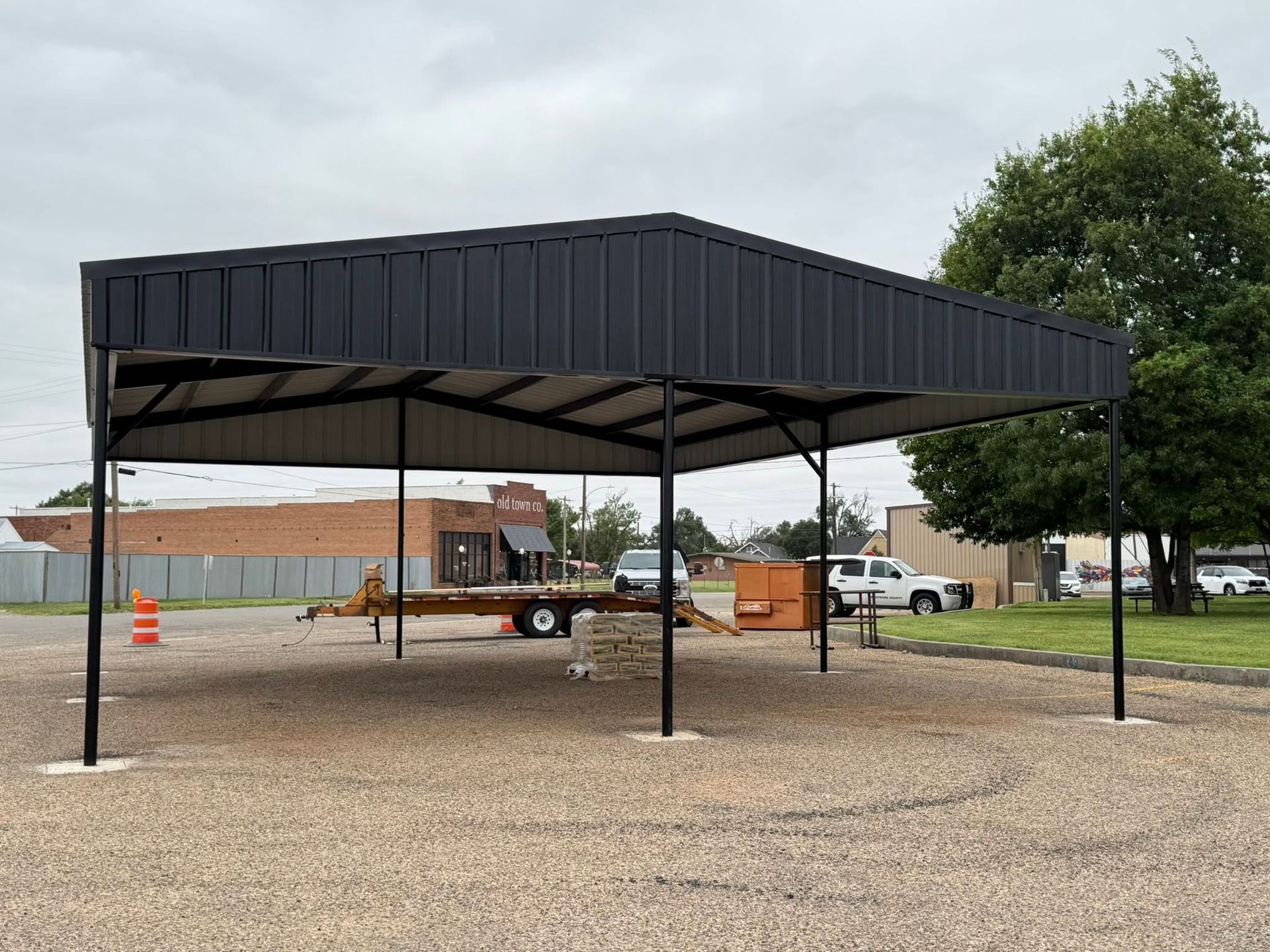 Black metal pavilion shelter on gravel lot under cloudy sky