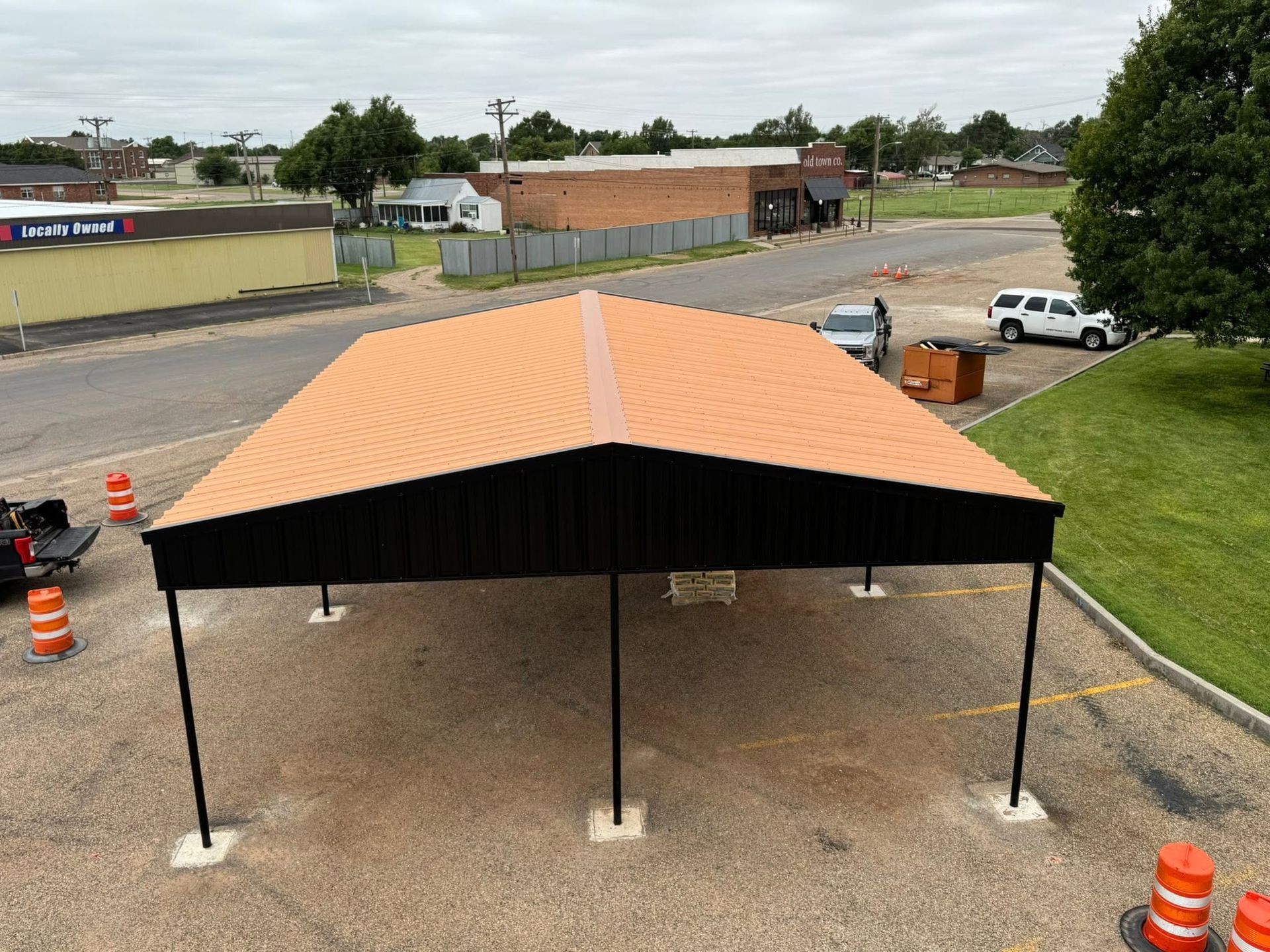 Orange-and-black canopy tent set up on gravel near a parking lot and road, with orange traffic barrels nearby
