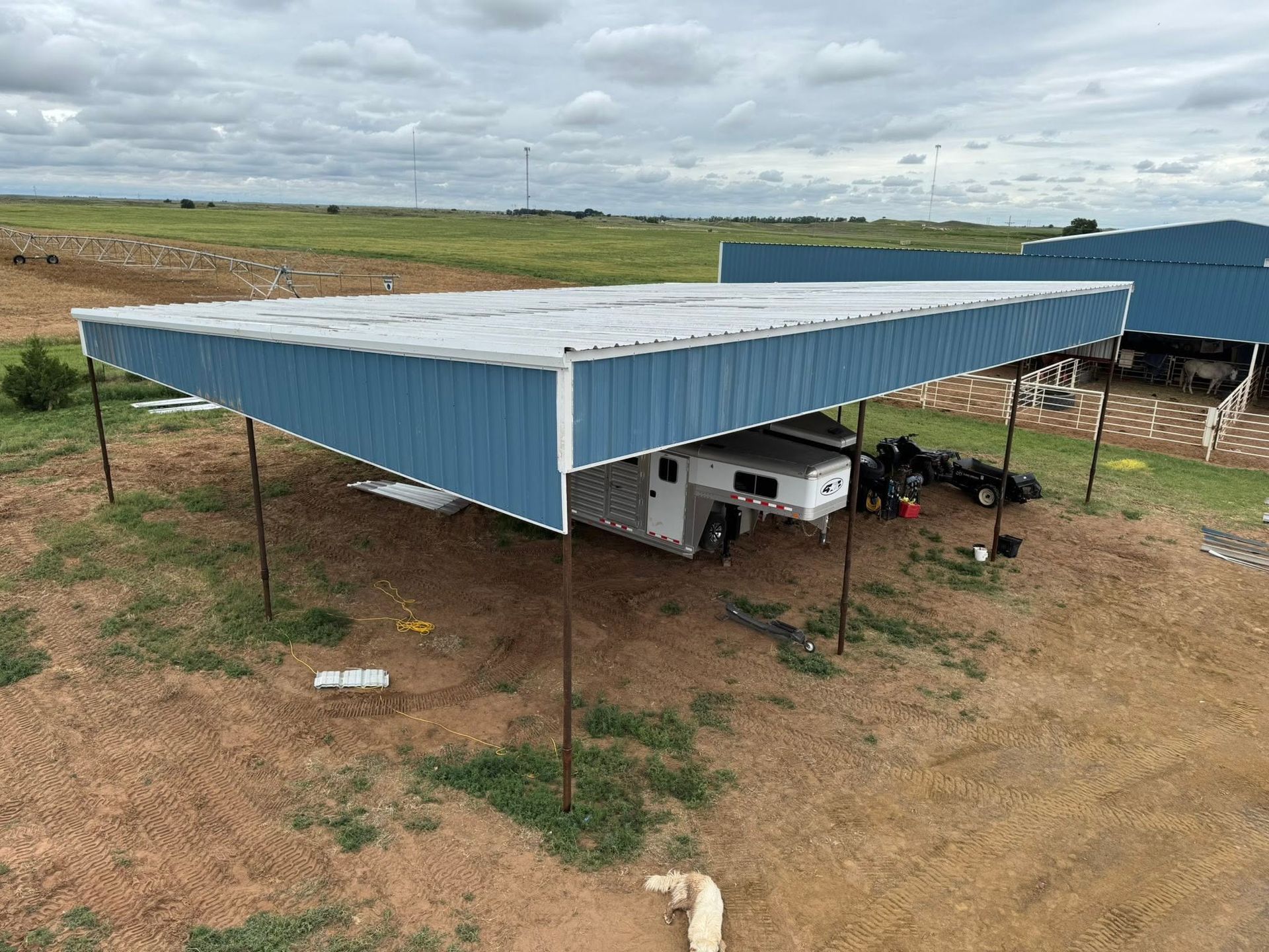 Blue metal carport on stilts sheltering a vehicle in a rural field under cloudy skies
