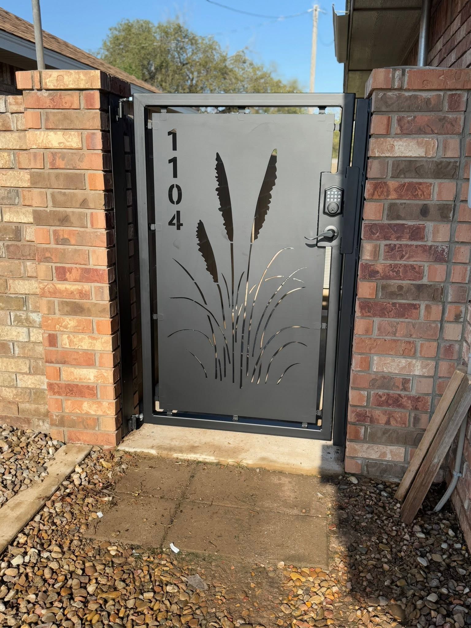 Black metal gate with decorative grass design between brick pillars, house number 1104.