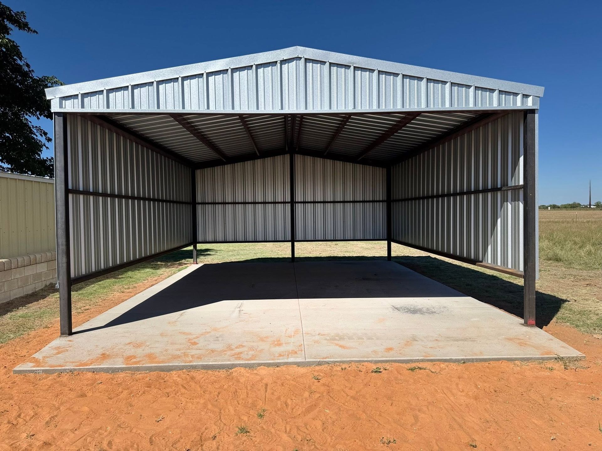Empty corrugated metal shed with a concrete floor in a dry open field.