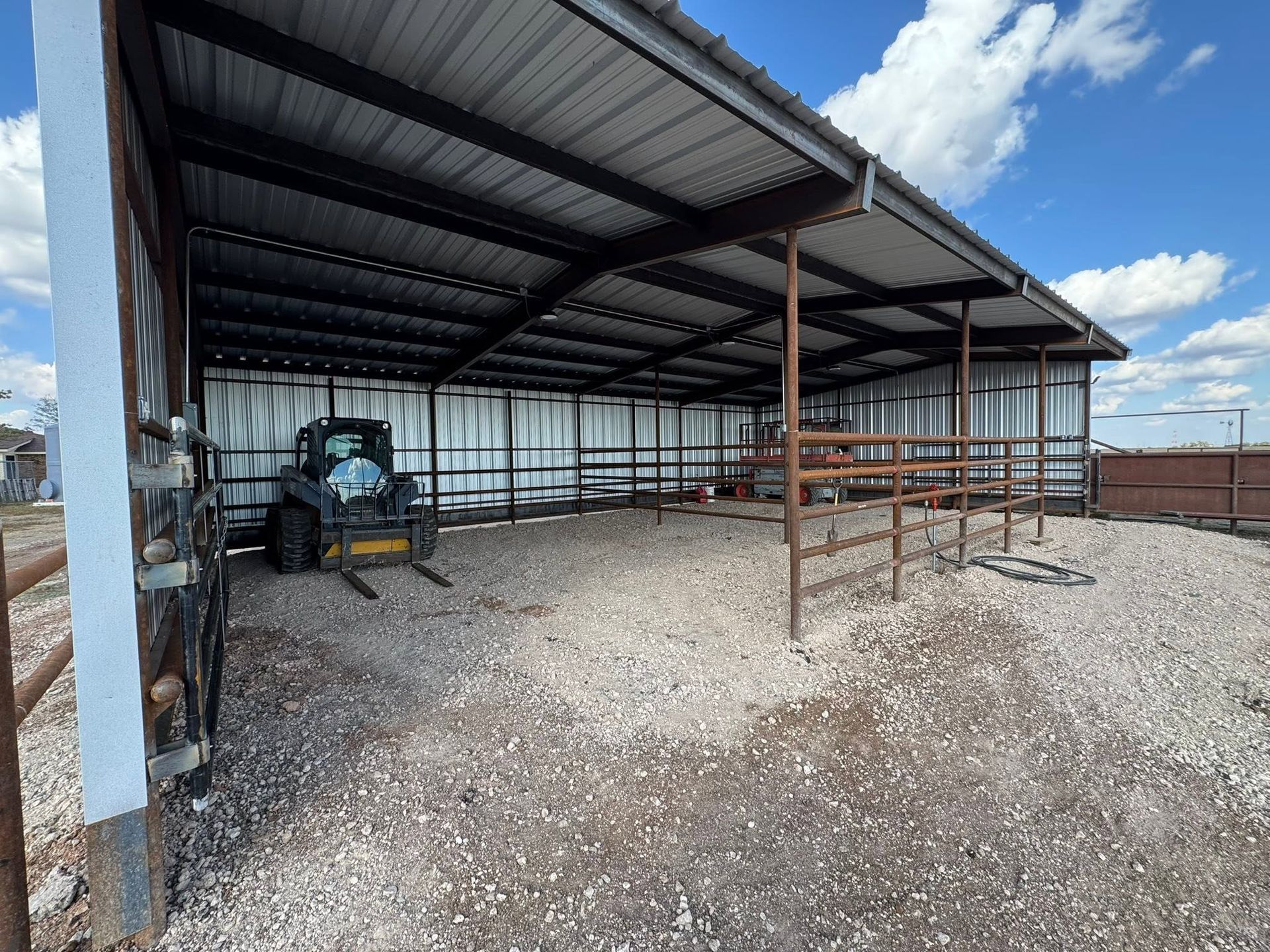 Open-sided metal livestock shelter on gravel, with a tractor inside under a cloudy sky.