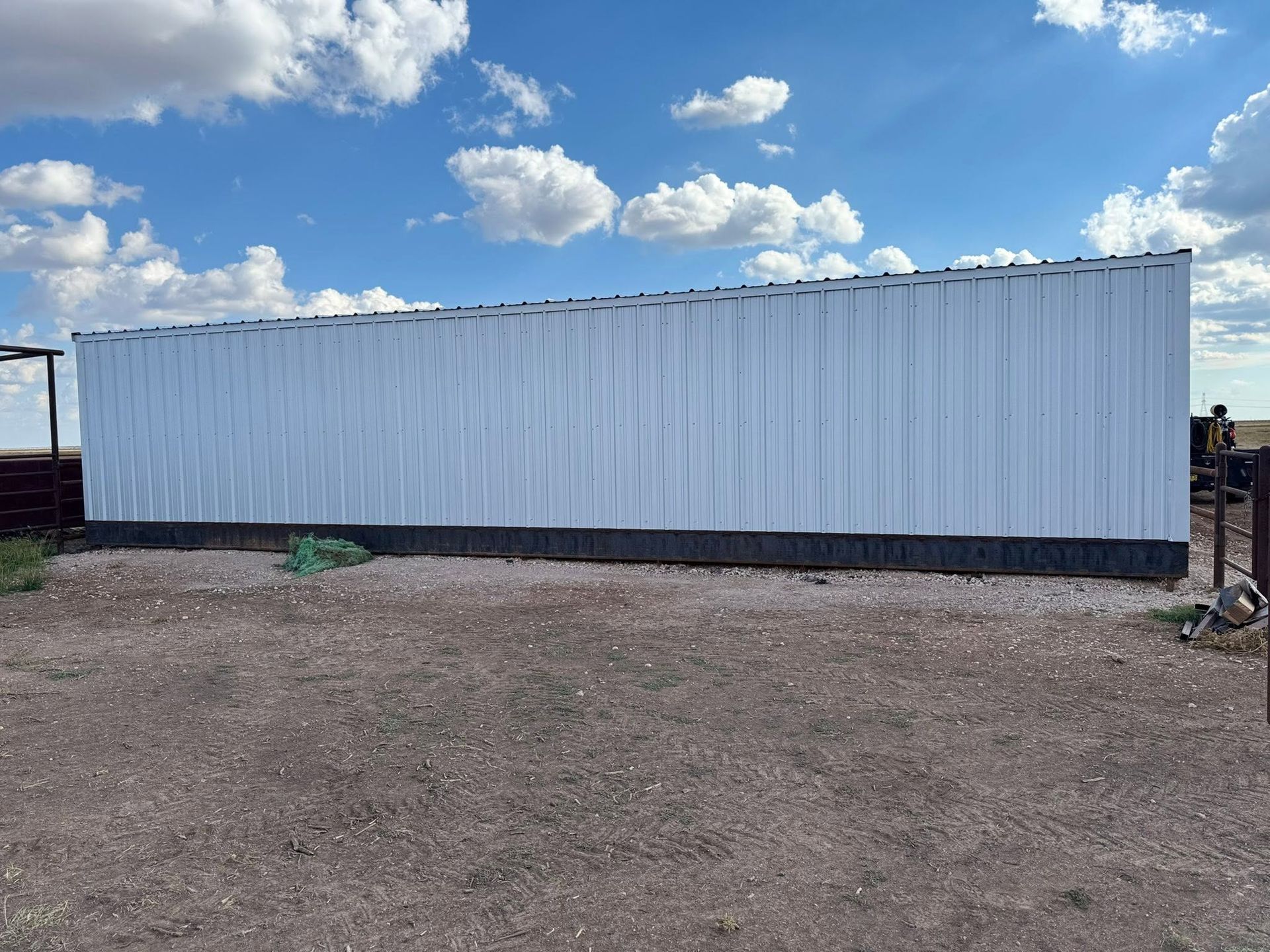 Long white shipping container on a dirt lot under a blue sky with clouds