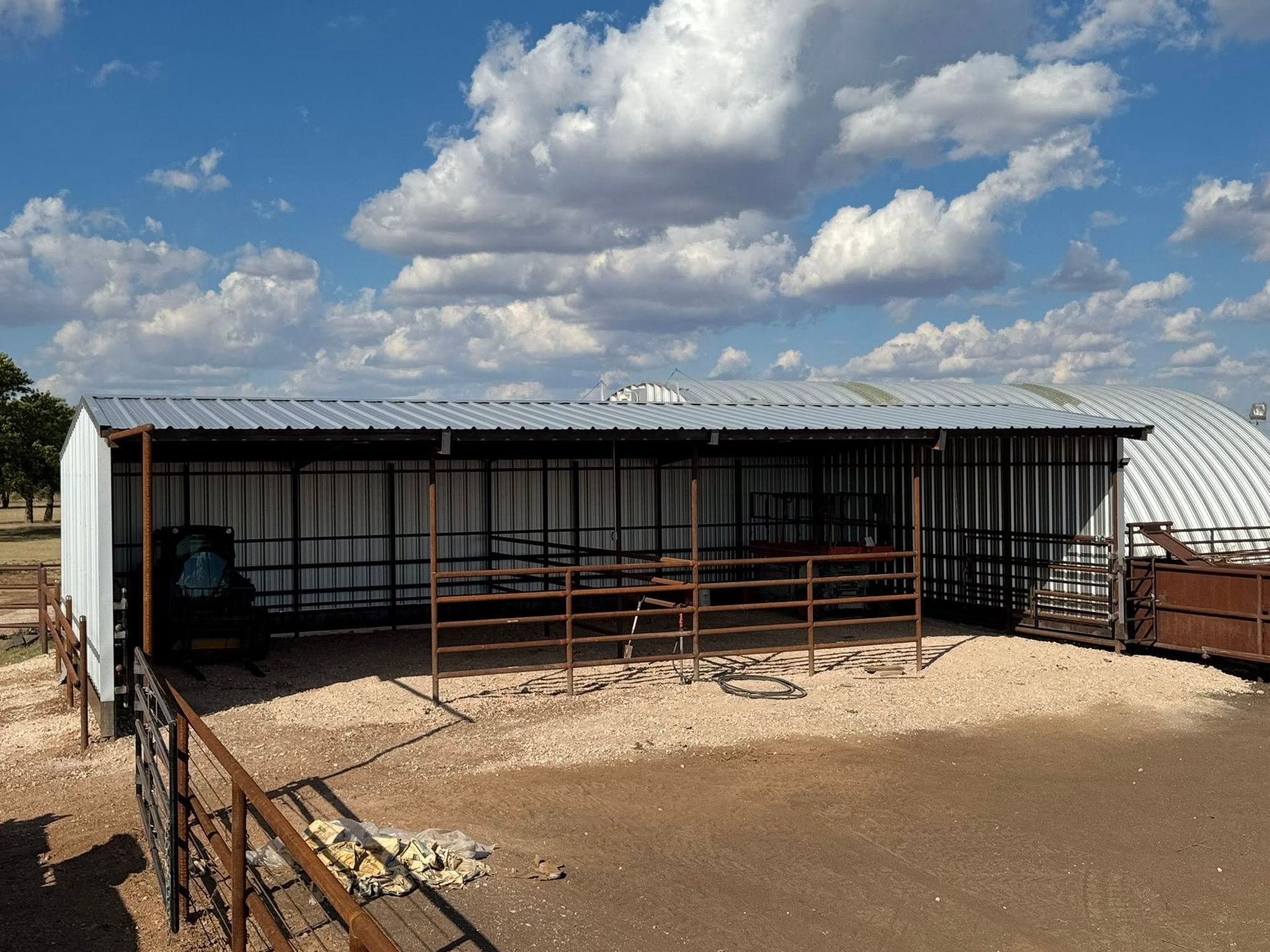 Covered livestock pen with metal fencing and a corrugated roof under a cloudy sky