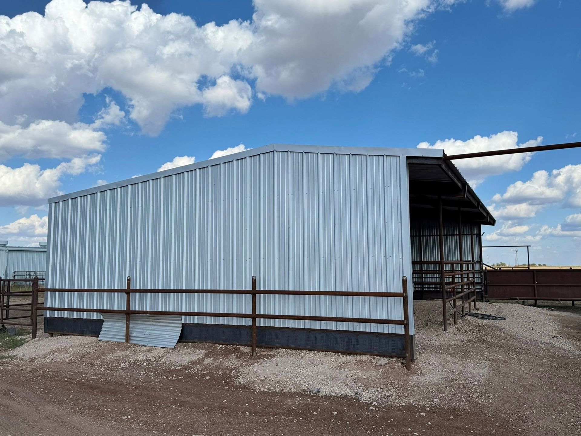 Corrugated metal shed in a gravel yard under a cloudy blue sky