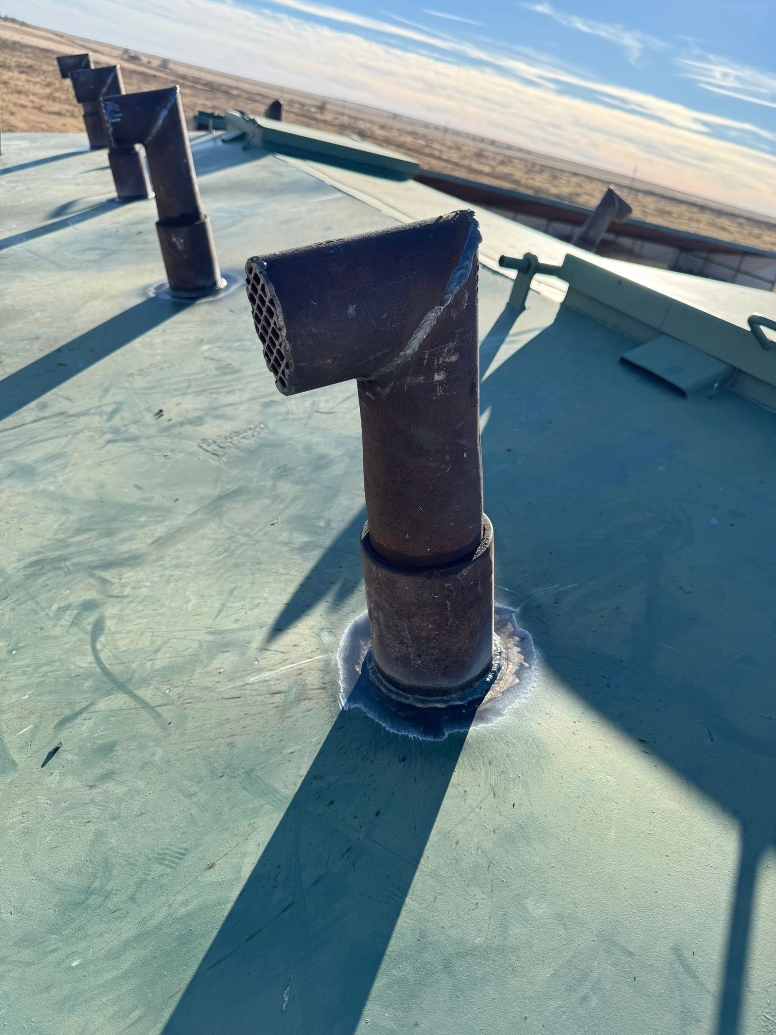 Roof vent pipes on a teal flat roof near the shoreline