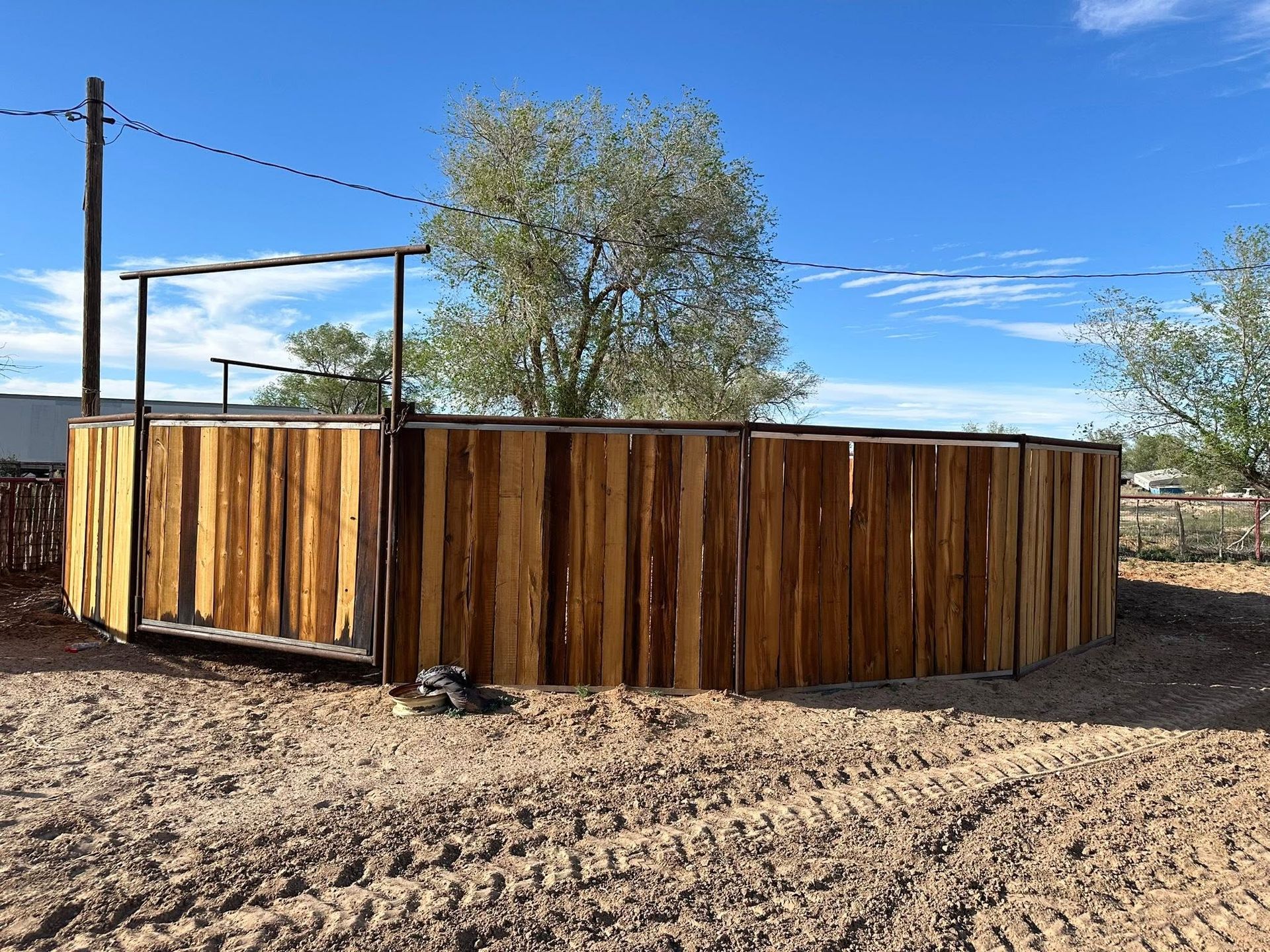 Round wooden livestock pen in a dry, rural yard under a clear blue sky