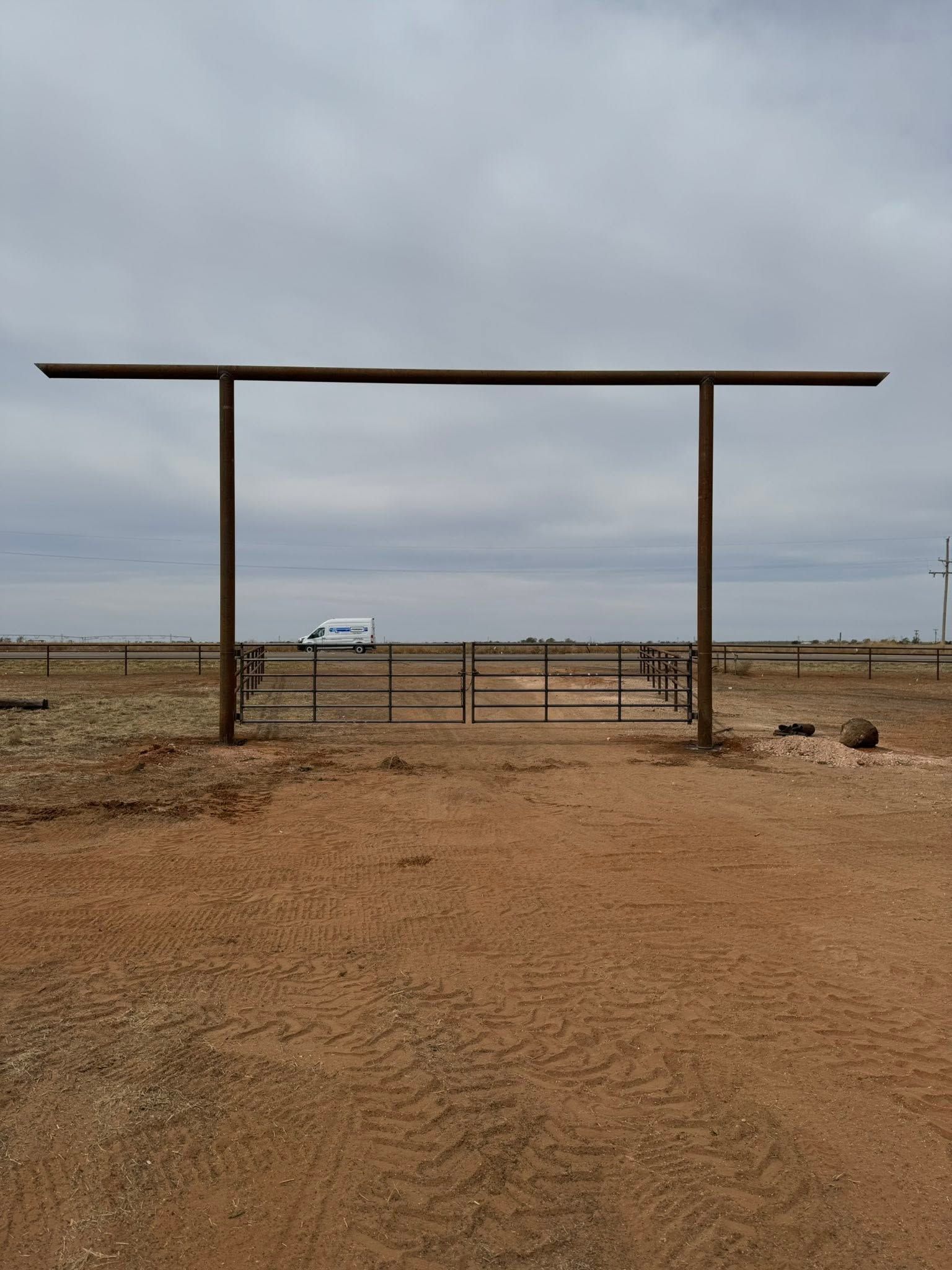 Desert entrance with a tall metal gate and fenced path under a cloudy sky