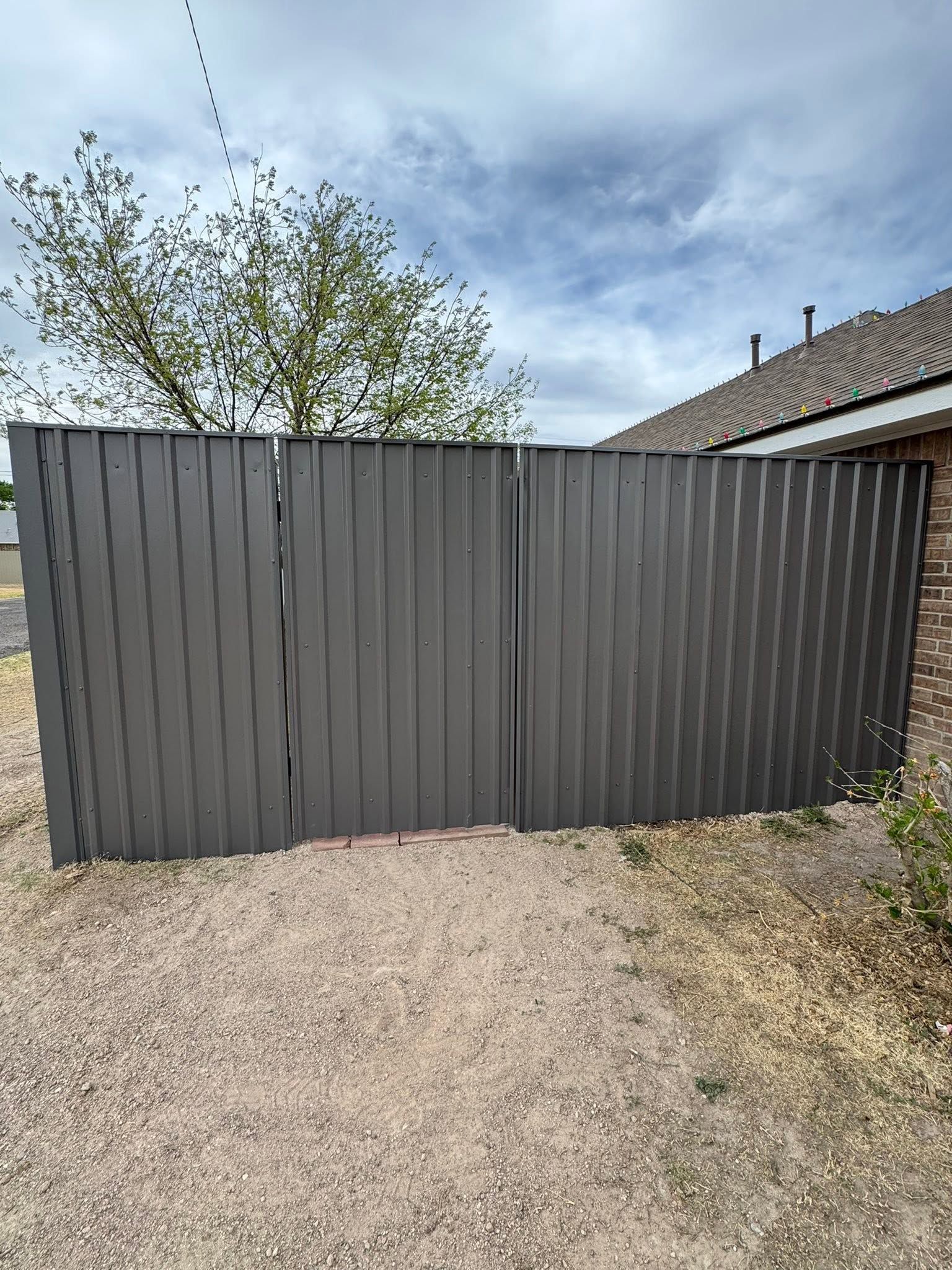 Gray metal fence gate blocking a gravel driveway under a cloudy sky.