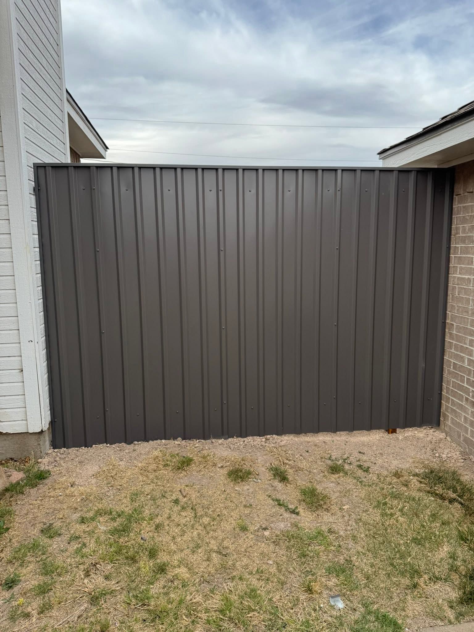 Dark brown corrugated metal gate between two houses above a gravel yard