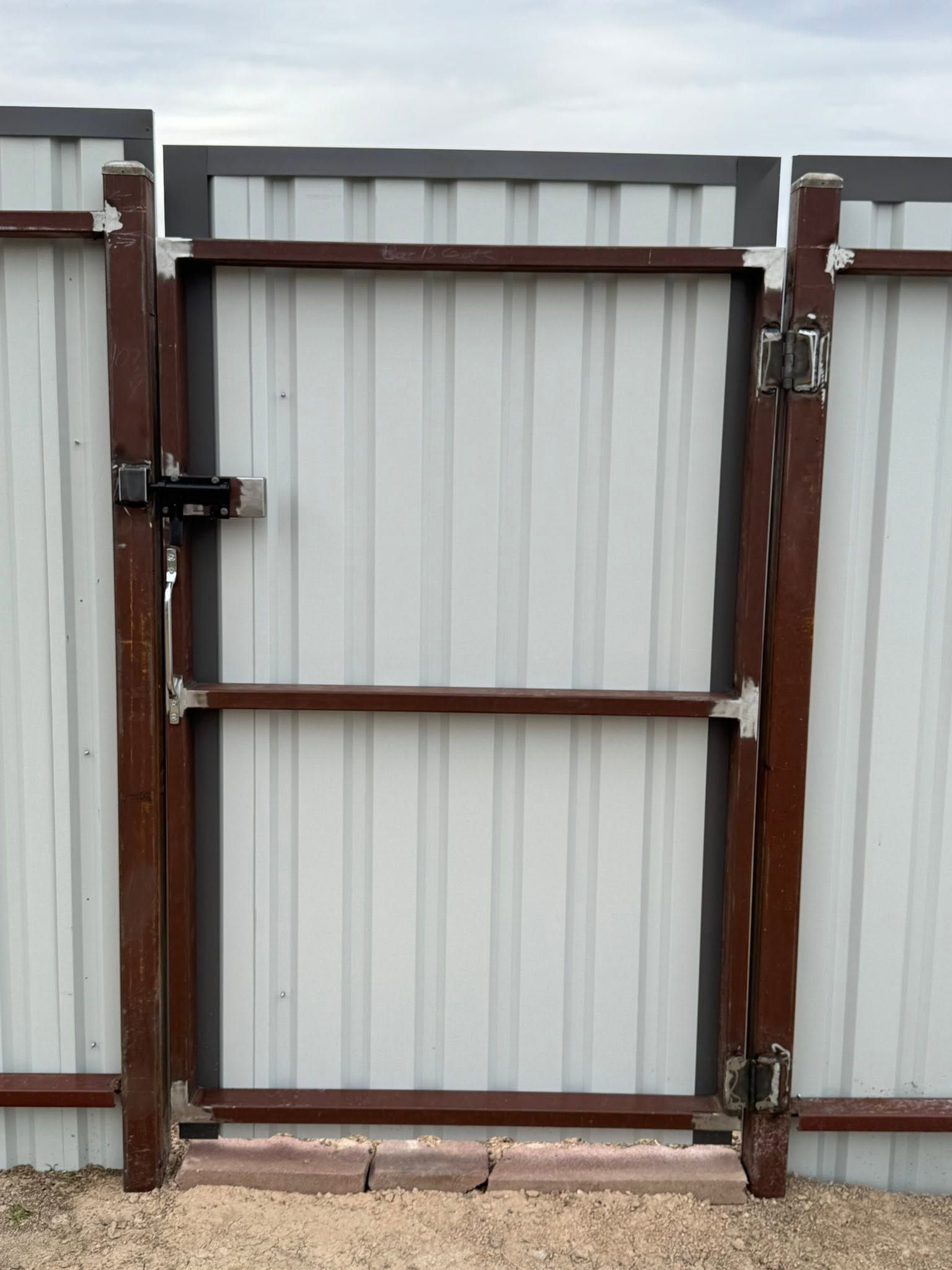 Closed corrugated metal gate with rust-colored frame and latch on a concrete surface