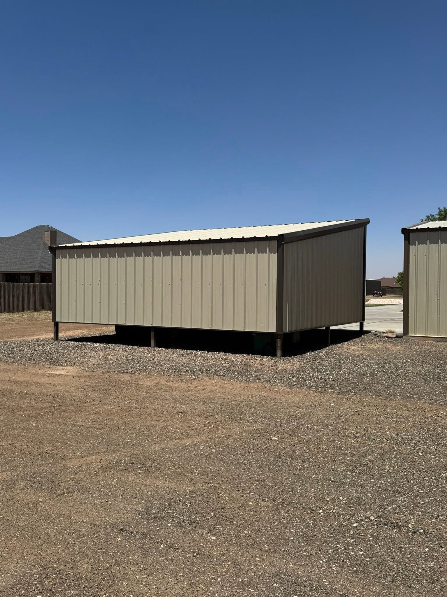 Small tan metal storage shed on gravel under a clear blue sky.