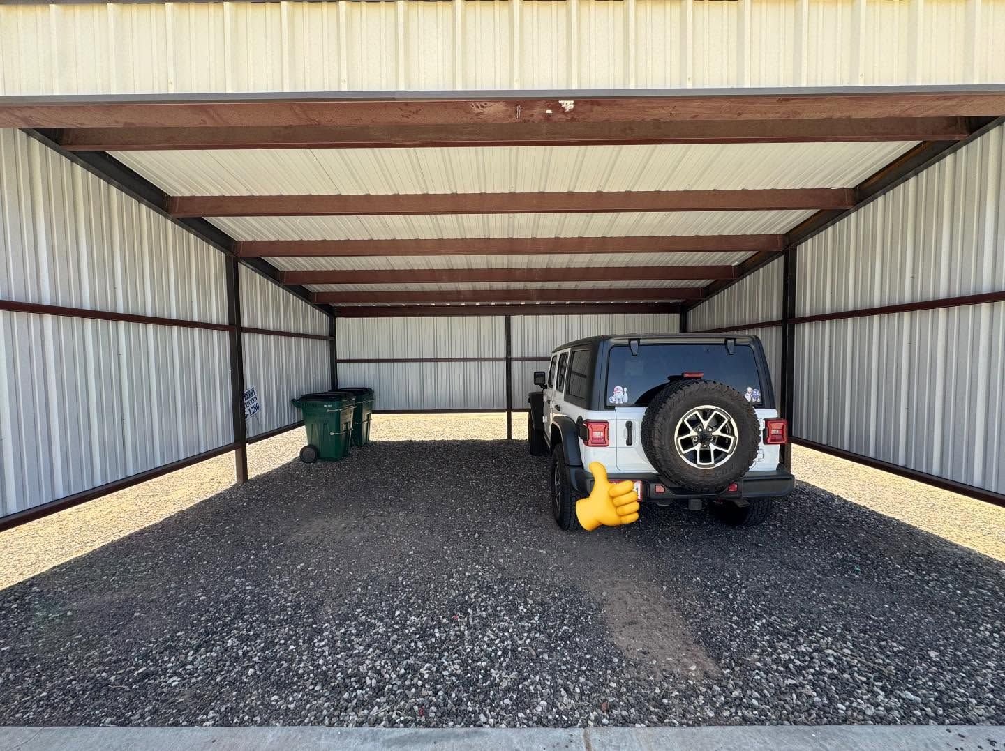 Covered gravel carport with a white SUV, trash bins, and a yellow jack on the right side.