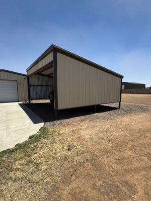 Small tan metal storage shed with a slanted roof on a gravel lot beside a concrete driveway.
