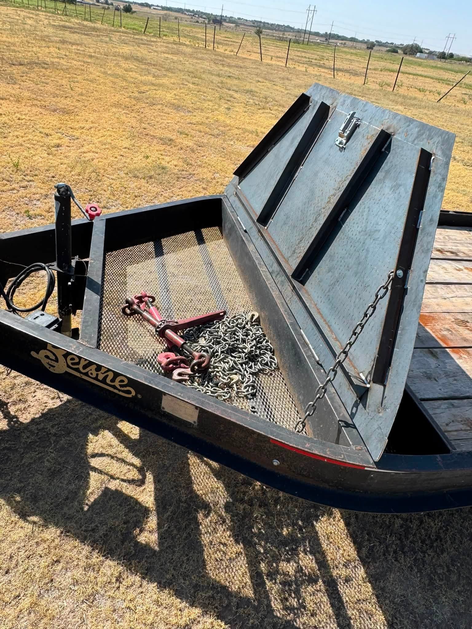Black trailer with a raised metal ramp loaded with gravel in a dry field