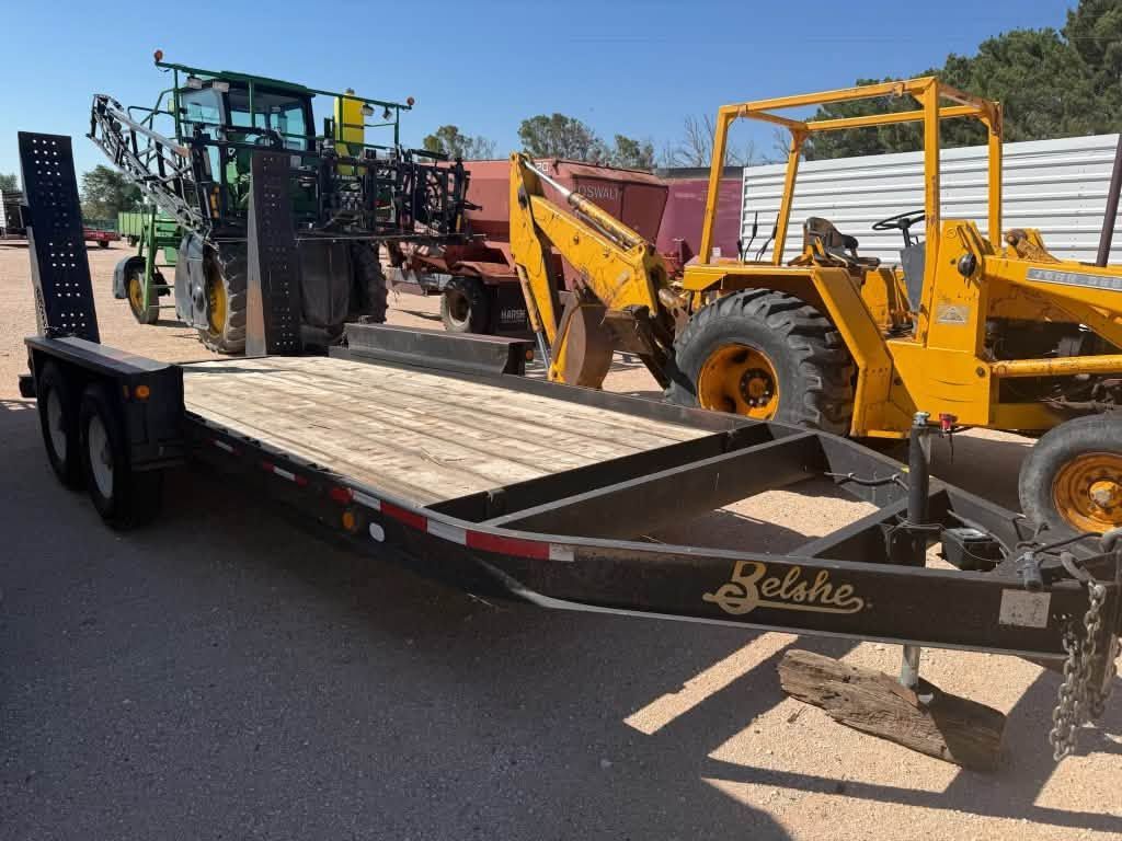 Flatbed trailer loaded with a yellow backhoe and other construction equipment on a sunny roadside.