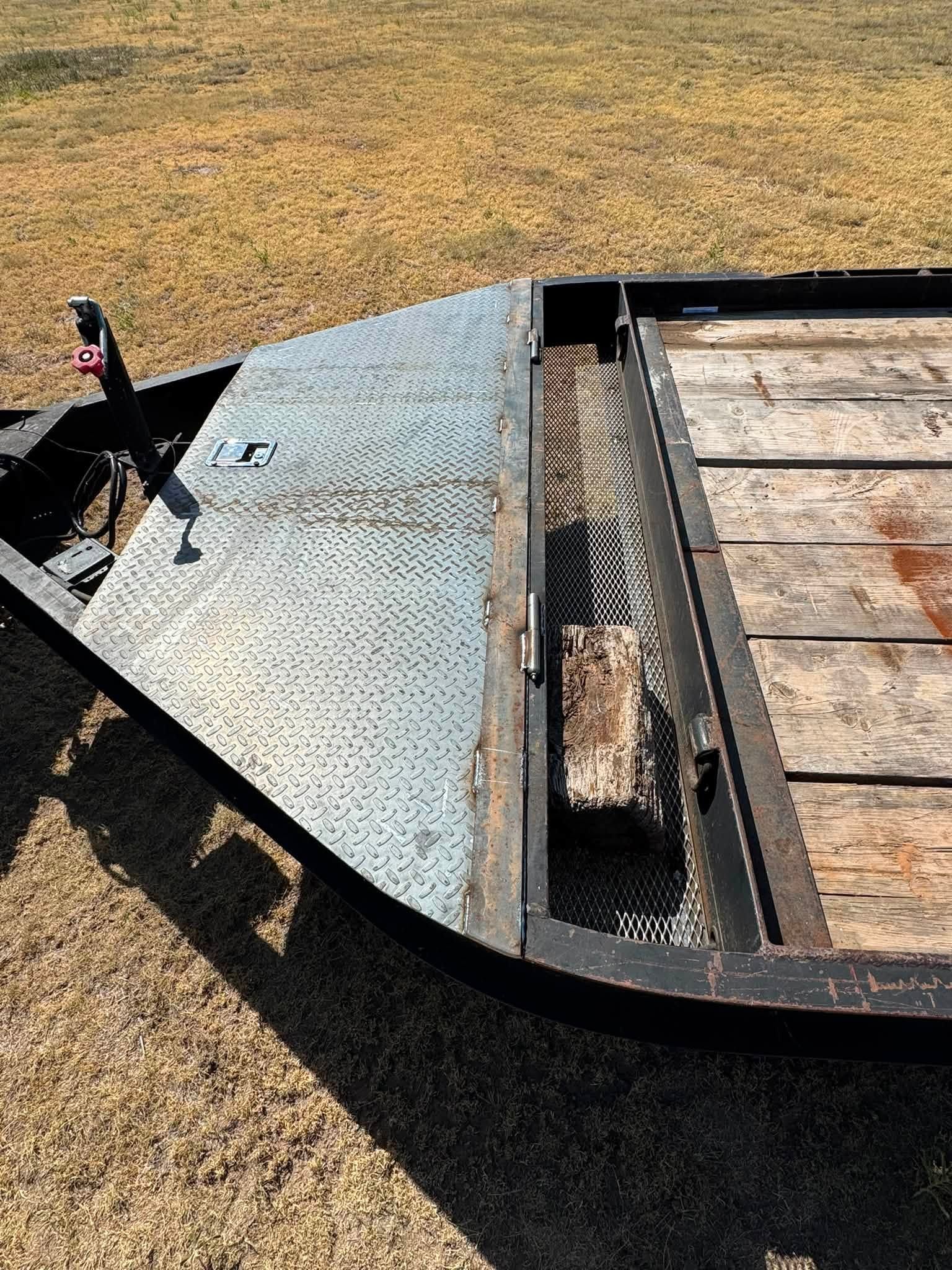 Open utility trailer with diamond-plate ramp and wood deck on dry grass