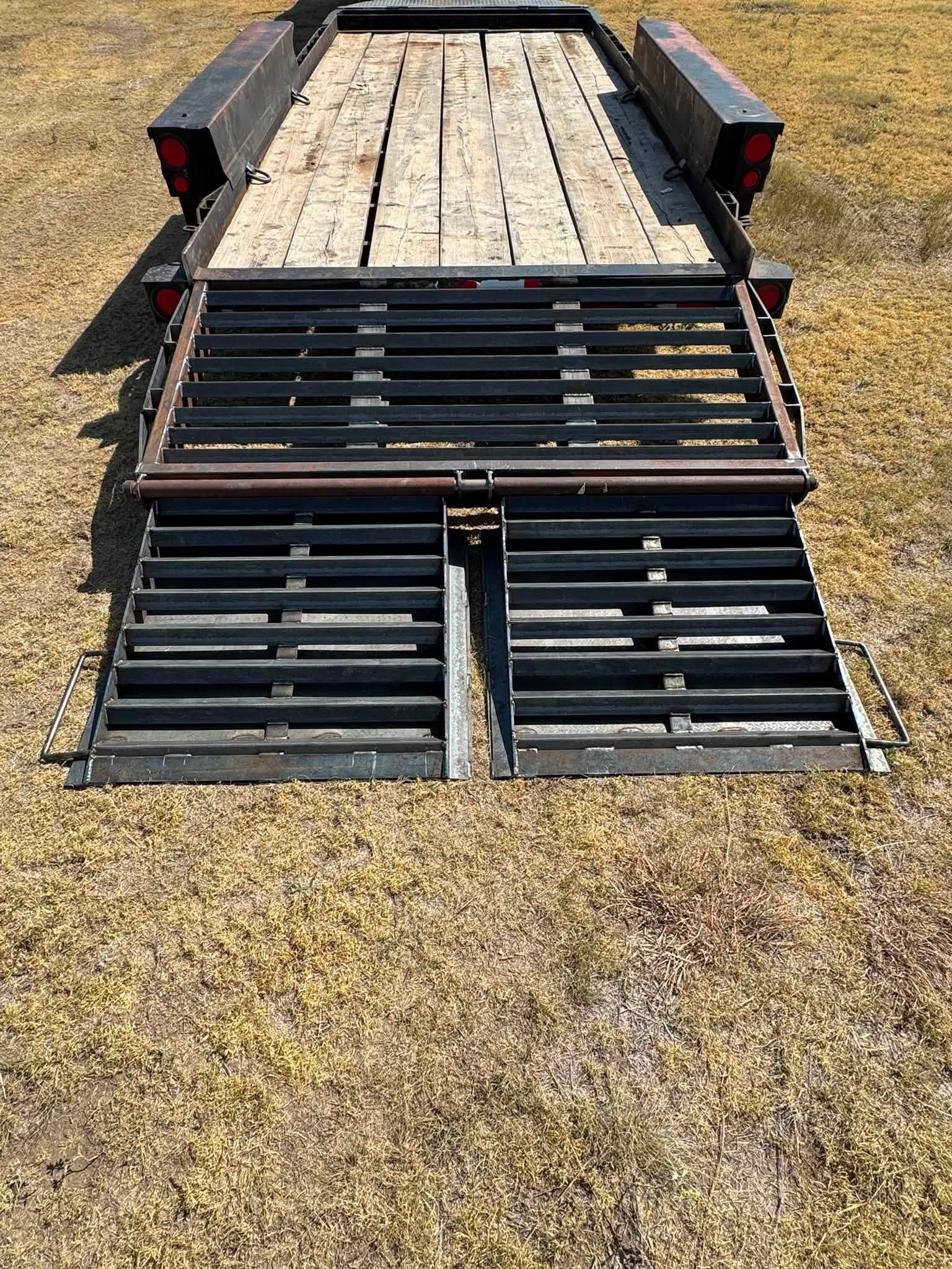 Folded black metal livestock trailer ramp on a gravel lot, with wood-planked bed and side rails.