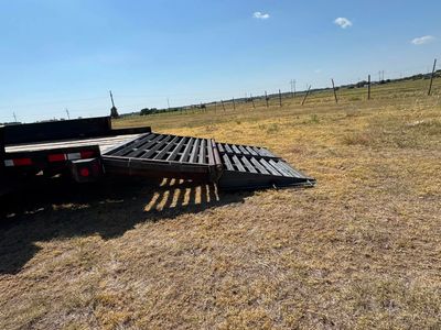 Flatbed trailer ramp lowered onto dry grassy field under a clear blue sky