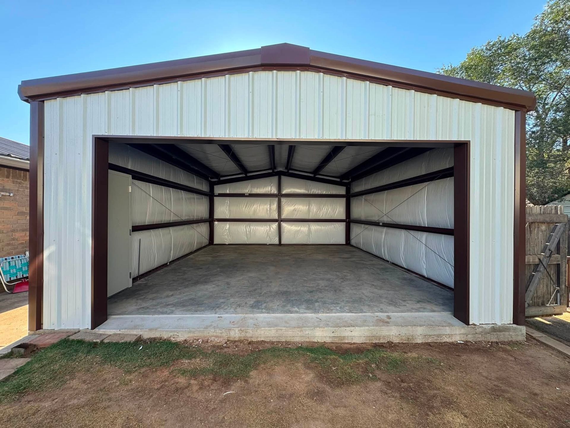 Open metal garage with white walls and brown trim, viewed from the front, empty inside.