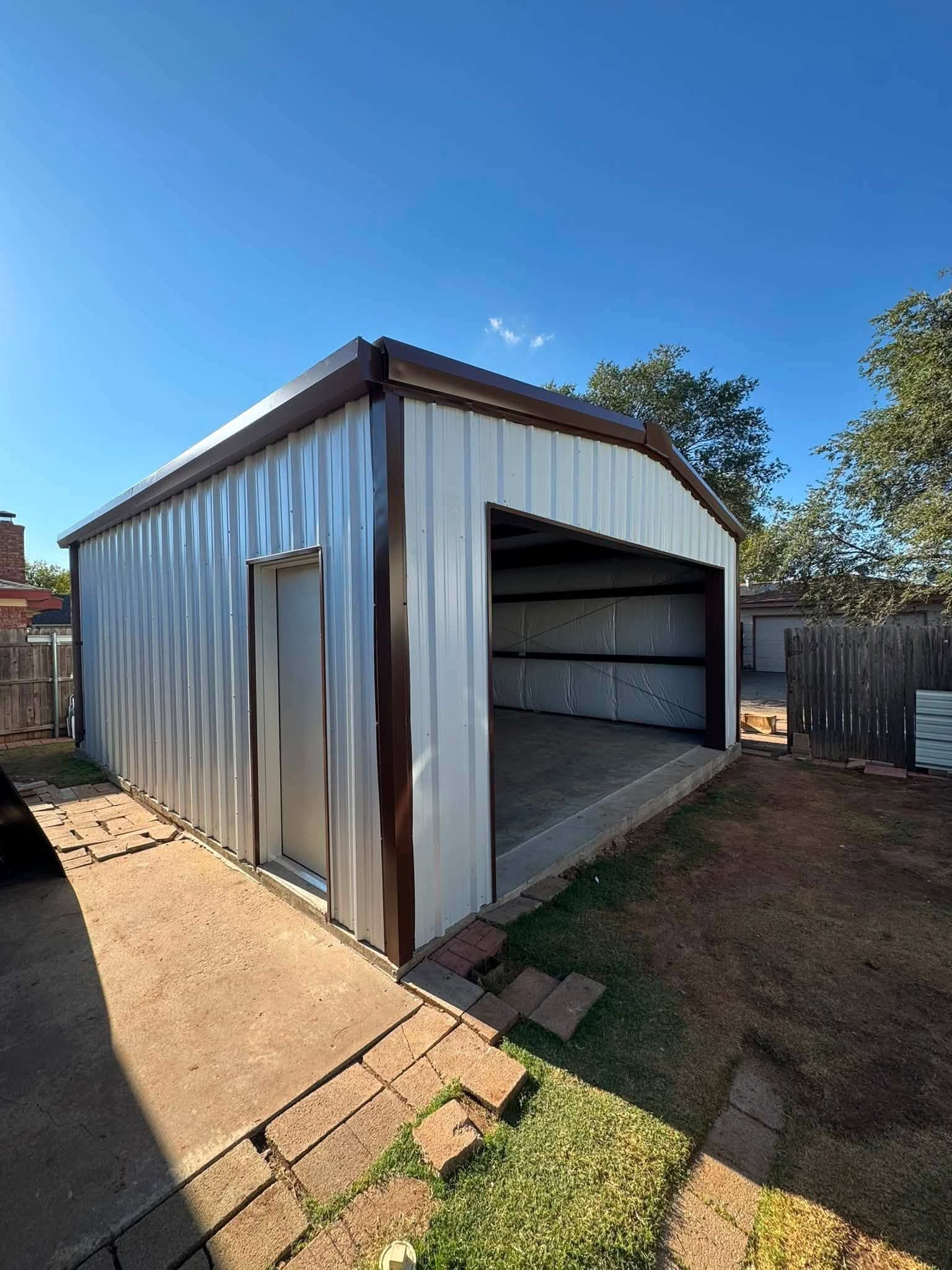 Small metal storage shed with an open garage-style door in a sunny backyard.