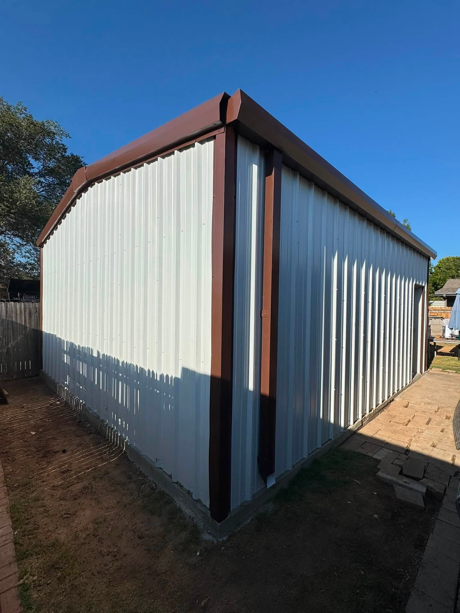 Small corrugated metal shed with white walls and rust-colored trim in a sunny yard