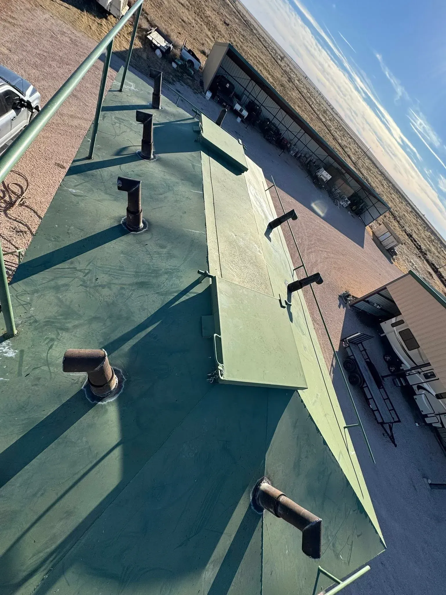 Roof with green shingles and skylights beside a long white building on a sunny day
