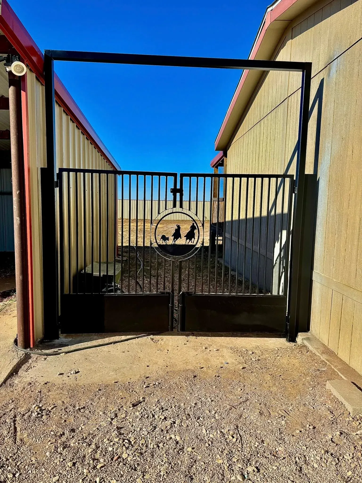Gated entrance to a narrow passage between tan walls under a bright blue sky