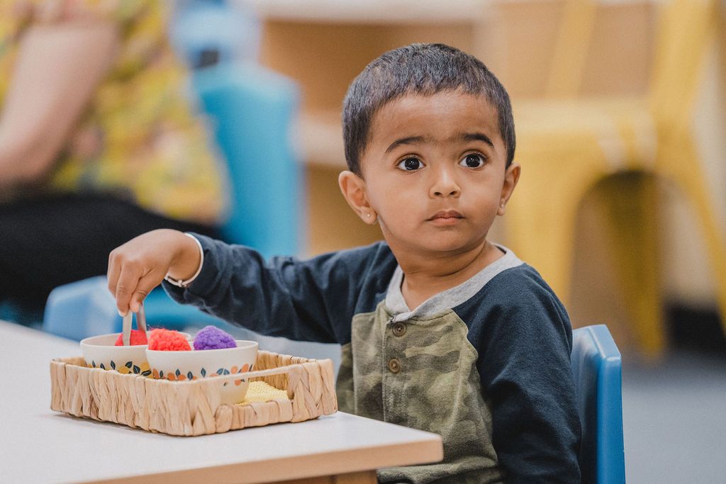 a young boy sits at a table with a basket of toys