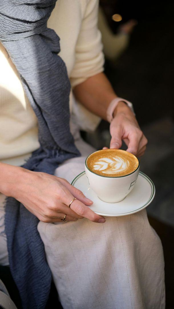 A woman is holding a cup of cappuccino on a saucer.