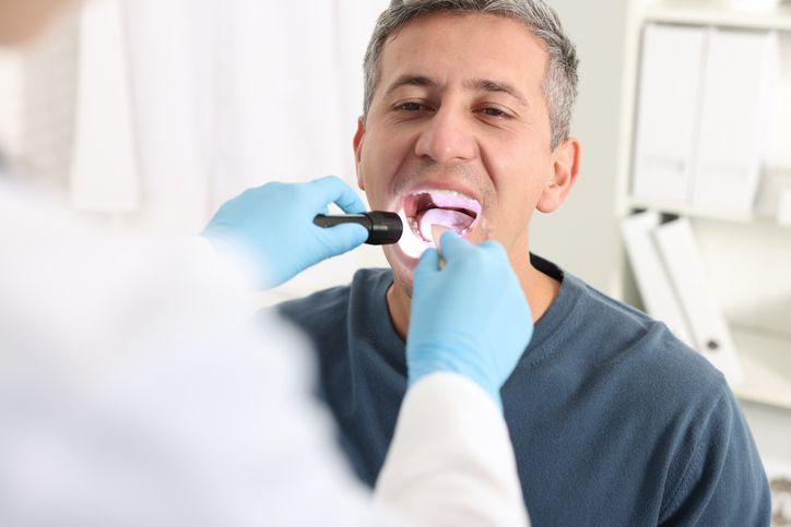 Dentist examining a patient’s open mouth with a dental mirror and blue gloves