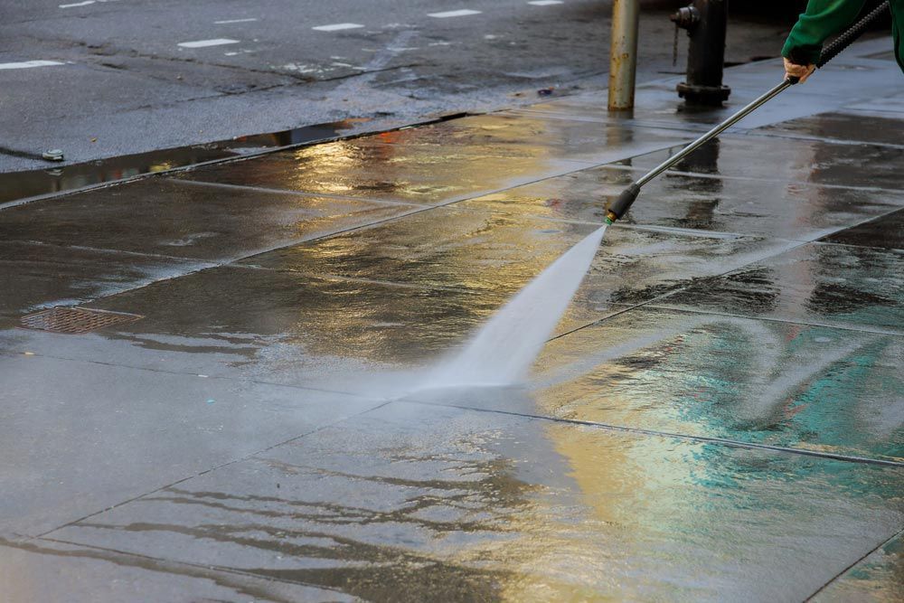 Person Power Washing a Wet Sidewalk, Creating a Stream of Water — Cairns Bin Cleaning In Parramatta Park, QLD