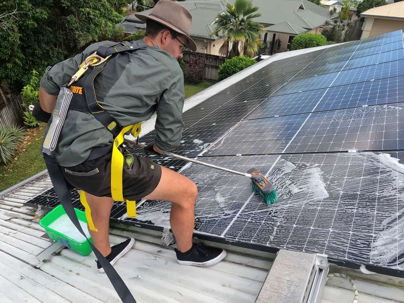 A Man Is Cleaning Solar Panels on The Roof of A House — Cairns Bin Cleaning In Parramatta Park, QLD