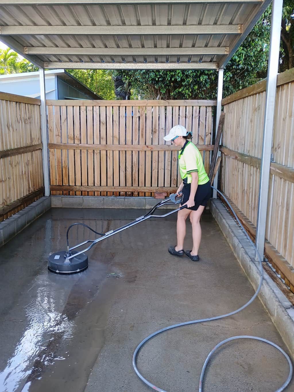A Woman Is Using a Pressure Washer to Clean a Driveway — Cairns Bin Cleaning In Parramatta Park, QLD