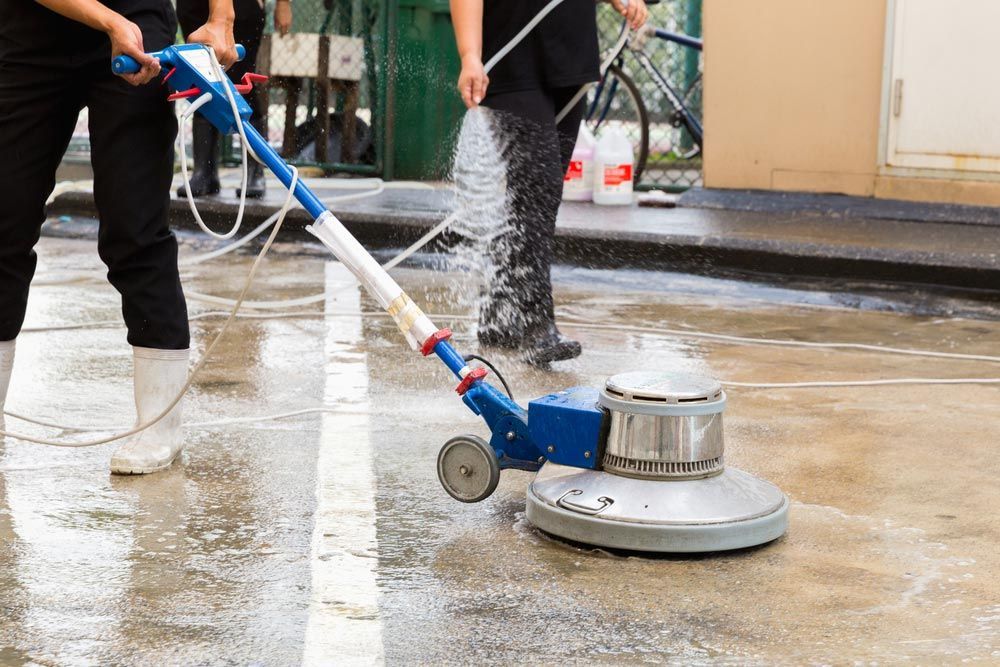 People Cleaning Concrete With a Floor Buffer Outdoors — Cairns Bin Cleaning In Parramatta Park, QLD