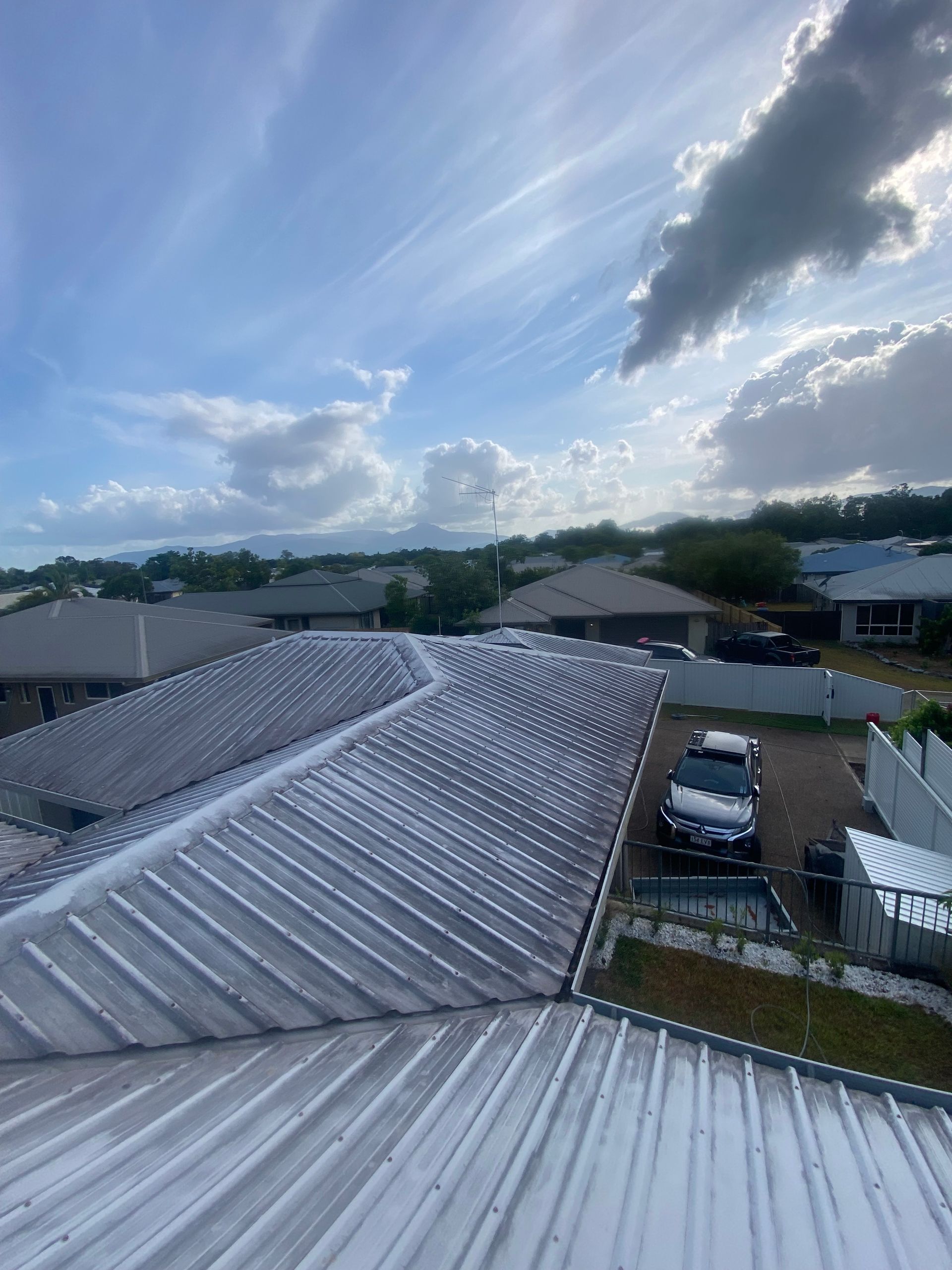 A Person Is Cleaning a Gutter of Leaves from A Roof — Cairns Bin Cleaning In Parramatta Park, QLD