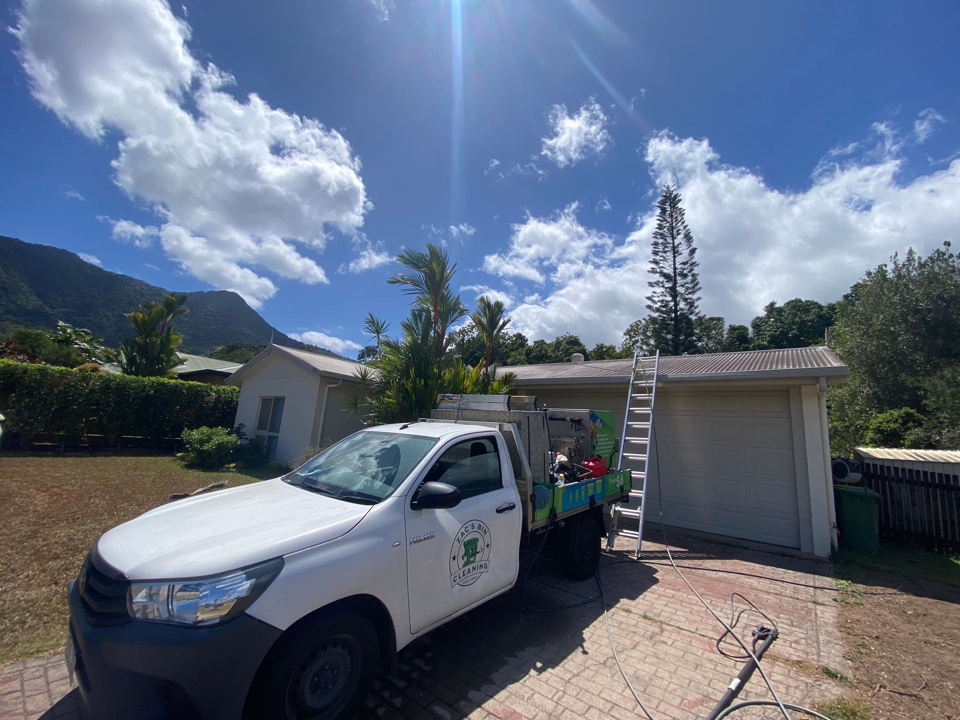 A Man Pressure Washes the Exterior of a White Garage Door and Trim — Cairns Bin Cleaning In Parramatta Park, QLD