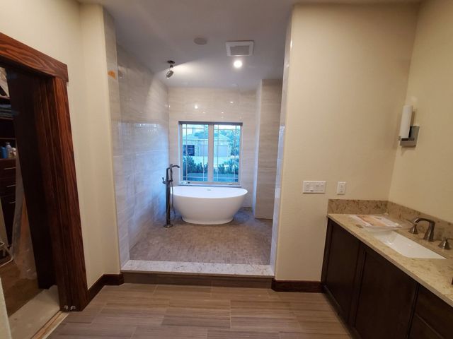 Bathroom with freestanding tub in tiled alcove, window view, and vanity on the right.