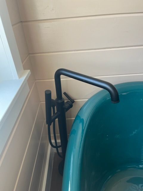 Turquoise tub with black grab bars beside a tiled bathroom wall and window nook