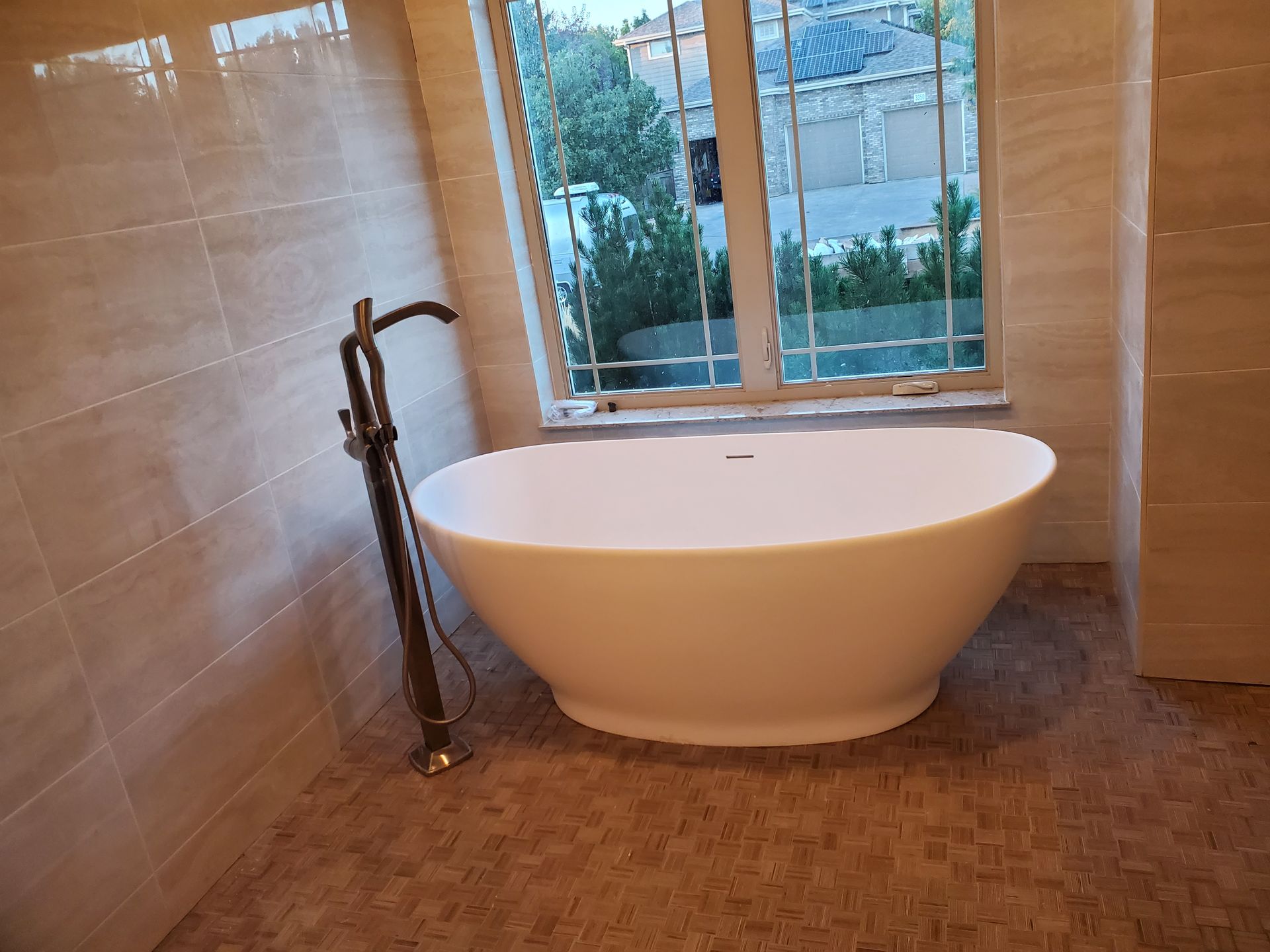 Modern bathroom with a freestanding white tub beside a window and dark floor-mounted faucet.