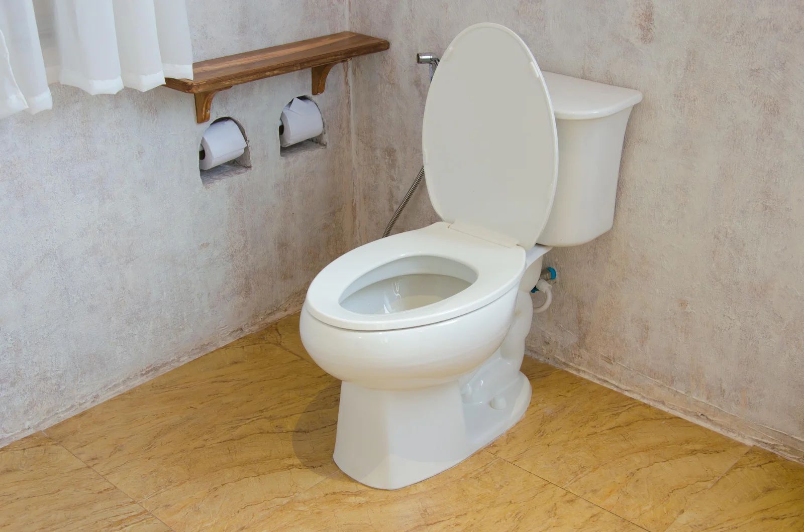Bathroom with a white toilet, wooden toilet paper shelf, and beige tile floor.