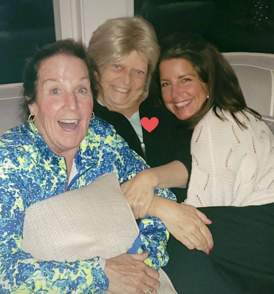 Three women are posing for a picture and one has a heart on her shirt