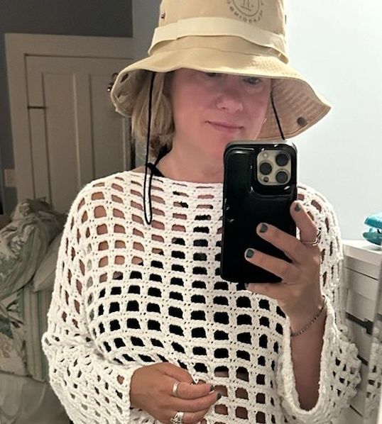 A woman wearing a hat is taking a picture of herself in a mirror.
