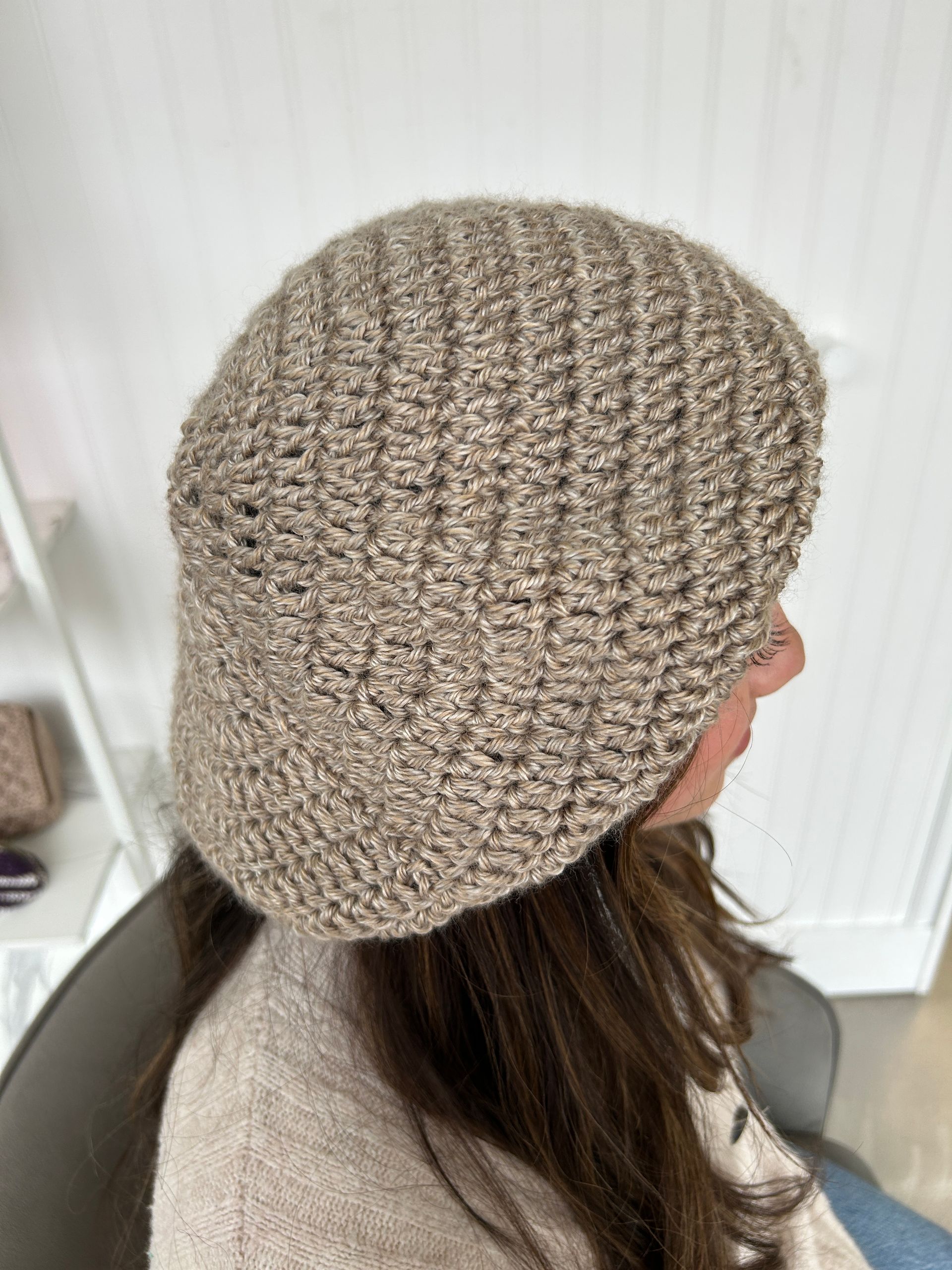 Person wearing a light brown knitted hat, angled side view.