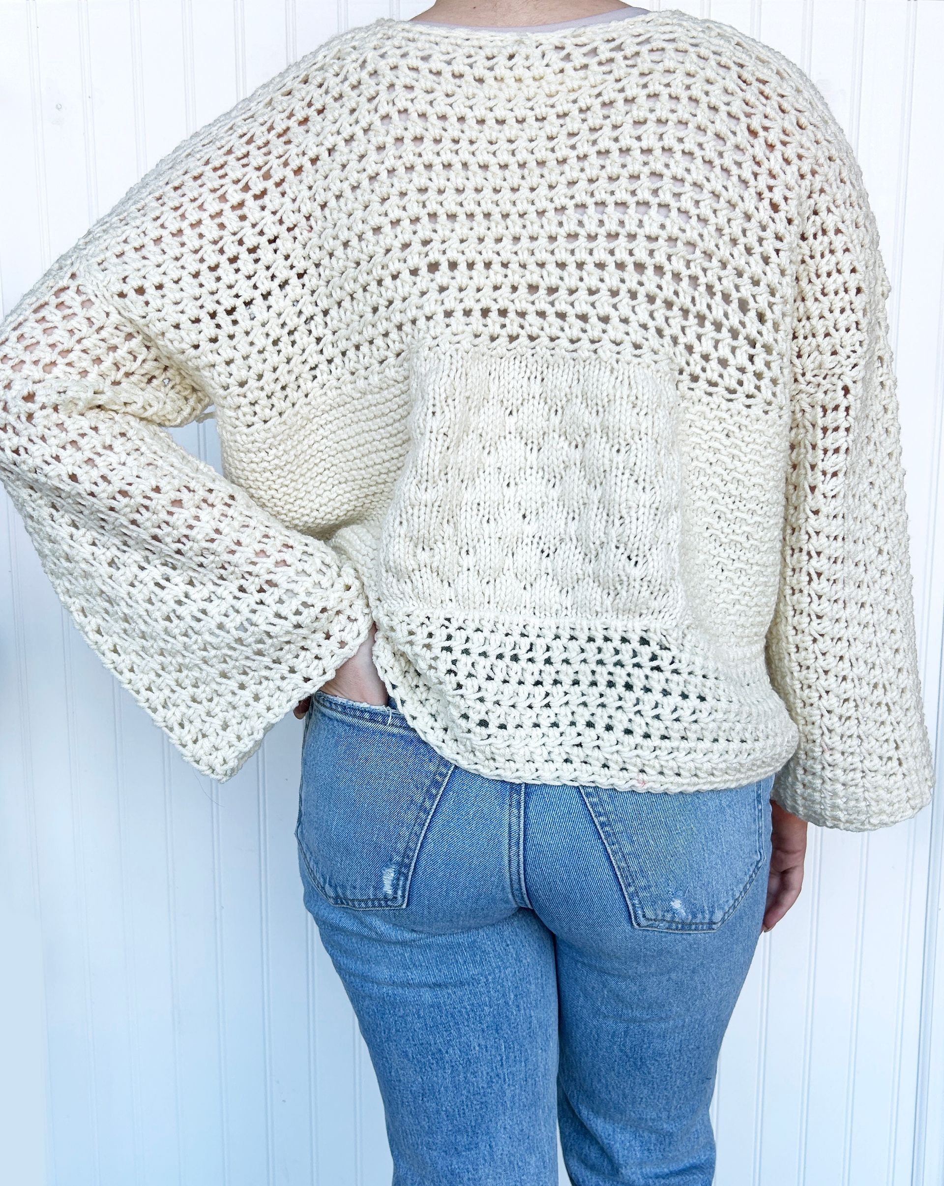 A woman is wearing a crocheted sweater and jeans.