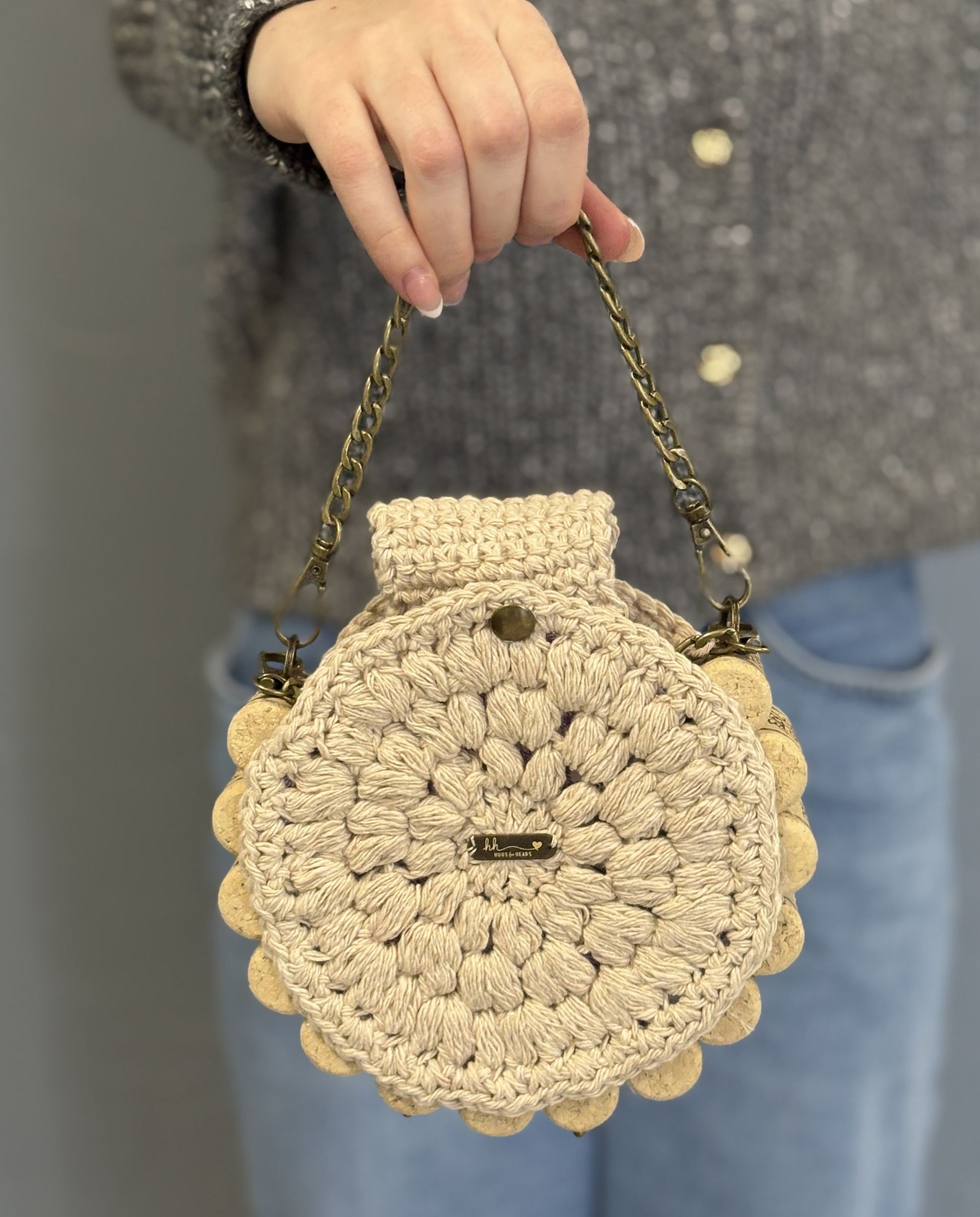 A person holding a beige crocheted seashell-shaped handbag with a gold chain strap.